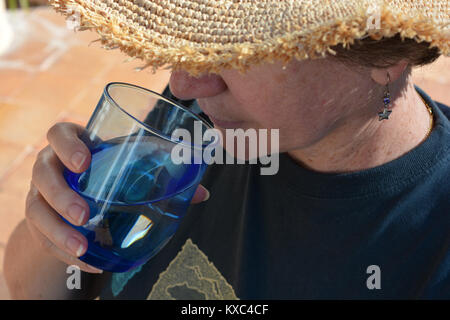 Femme à l'extérieur, portant un chapeau de paille et de boire un verre d'eau Banque D'Images