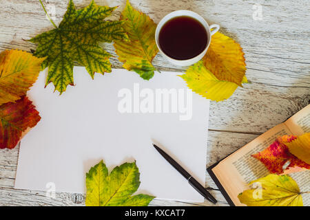 Feuille de papier blanc avec un stylo et une tasse de thé sur un fond en bois blanc avec les feuilles d'automne et d'une partie d'un livre ouvert Banque D'Images