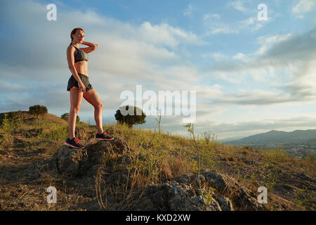 Low angle view of woman with hand behind head debout sur les rochers de la colline contre ciel nuageux Banque D'Images