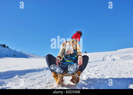 Photo de heureux la mère et l'enfant dans la neige avec une luge dans un jour d'hiver ensoleillé Banque D'Images