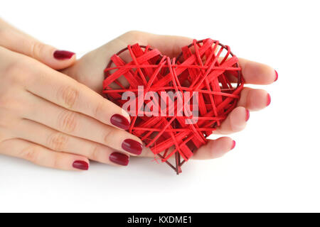 Coeur rouge en osier dans woman's hands sur fond blanc. Coeur gros plan dans la main de girl with red manicure. Happy Valentines Day, love concept. Banque D'Images