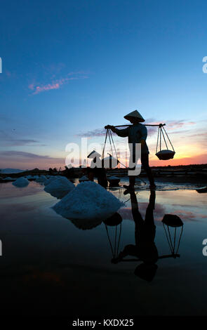 Les travailleurs de sexe féminin la récolte du sel de l'eau salée près des étangs à Doc Let, Vietnam. Ils commencent à travailler bien avant le lever du soleil, d'éviter la plupart de la chaleur Banque D'Images