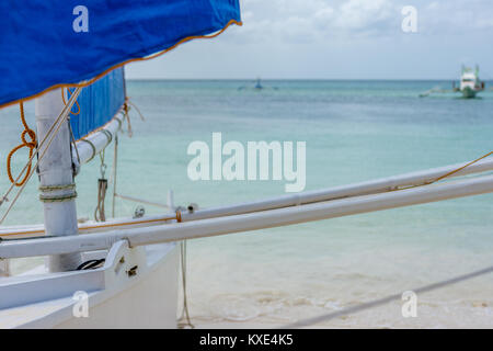 L'accent Premier plan d'un bateau à voile Philippines sur la plage donnant sur une mer calme avec des bateaux de la pompe à l'arrière du terrain. Banque D'Images