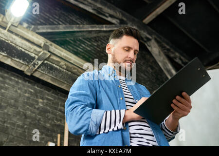 Low angle portrait of handsome man writing on clipboard barbu tout en travaillant dans l'élaboration d'atelier Banque D'Images