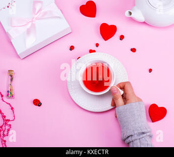 Les baies de la viorne thé dans une tasse en céramique blanche est la tenue d'une main de femme sur une table rose, vue du dessus Banque D'Images