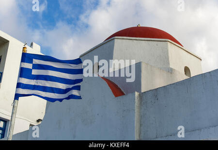 Mykonos, Grèce drapeau grec par église blanchie à. La vue quotidienne de brandir le drapeau grec dans le vent par une église orthodoxe au bord de la ville de Mykonos. Banque D'Images