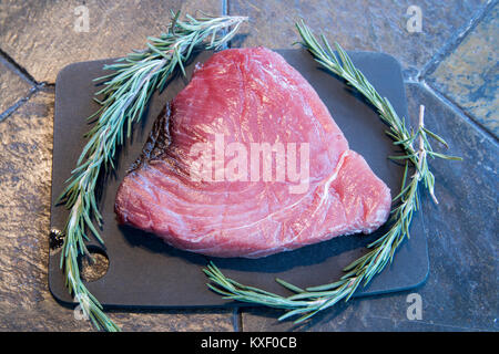 Steak de thon rouge cru avec des brins de romarin sur une planche à découper sur l'ardoise d'examen. Banque D'Images