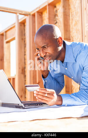 Un homme sur son téléphone à un ordinateur portable à l'ordinateur et en utilisant sa carte de crédit. Banque D'Images