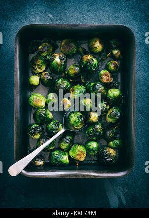 Brassica oleracea. Choux de Bruxelles rôtis dans une plaque de cuisson avec une cuillère sur fond d'ardoise. Vintage filtre appliqué Banque D'Images