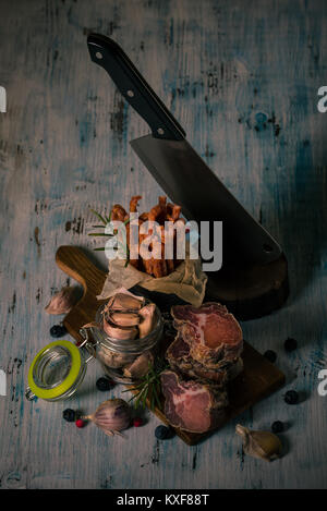 Photo verticale avec l'italienne empilés la viande provenant de porcs sangliers mis sur vintage planche en bois avec de l'ail, la couleur des baies, des saucisses sèches et peut en b Banque D'Images