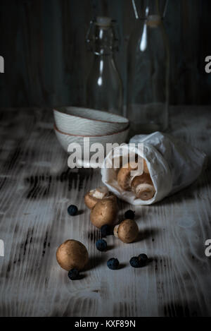 Photo verticale de plusieurs champignons comestibles brun avec bouchon. Champignons renversé sur vintage wooden board à partir de sac de papier avec quelques fruits secs. Deux bols Banque D'Images