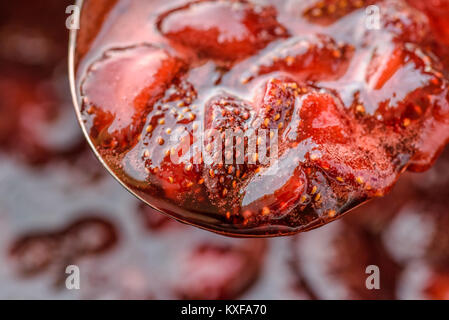 Accueil fraîchement cuit la confiture de fraise sur une cuillère avec des pièces de fraises dans une sauce brillante. Banque D'Images