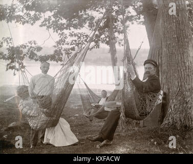 Photographie Ancienne vers 1905, se reposant dans un Shady Glen avec banc et hamacs, avec le Sasanoa River derrière eux. L'emplacement est dans ou près de Riggsville (maintenant) dans le Maine, Robinhood de Sagadahoc, USA. Banque D'Images