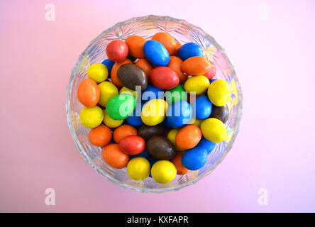 Bonbons multicolores dans un bol de cristal sur un fond uni Banque D'Images