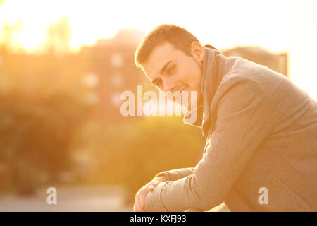 Portrait d'un homme heureux en vous regardant dans un balcon au coucher du soleil en hiver Banque D'Images