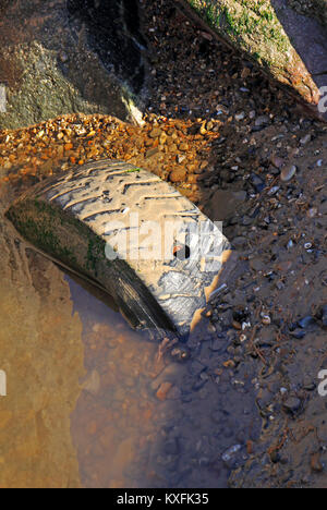 Un vieux pneu abandonné à moitié enfoui sur une plage à Norfolk, Angleterre, Royaume-Uni. Banque D'Images