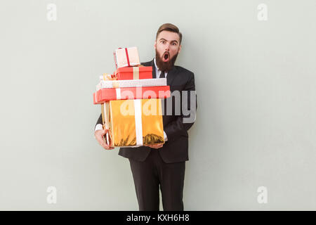 Funny man looking at camera avec visage choqué et holding gift boxes. Studio shot. Isolé sur fond gris Banque D'Images