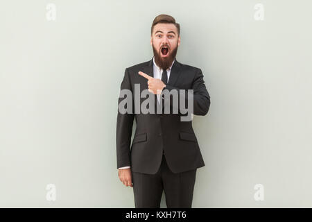 Beau présentateur de votre annonce. Happy young man in formalwear dirigés à l'écart debout contre un arrière-plan gris. Studio shot. Banque D'Images