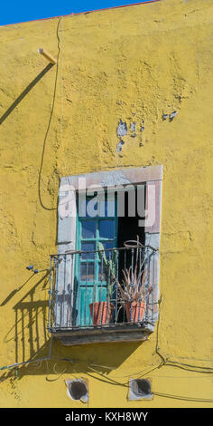 Vieille maison avec un mur extérieur jaune vif, un petit balcon avec une double porte avec un encadrement de porte en pierre, et les plantes en pots en argile, Guanajuato Banque D'Images