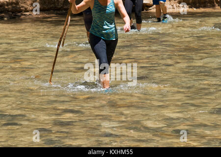 Female hiker marcher dans un ruisseau à l'aide d'un support. Habillés avec des leggings. Détail de la rivière. Banque D'Images