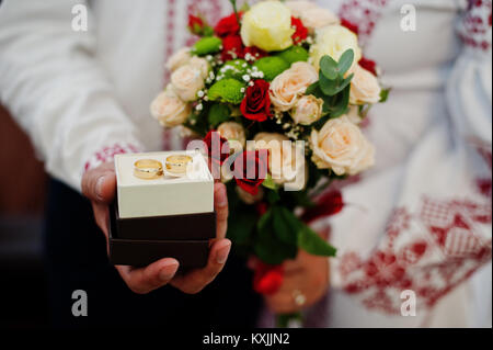 Photo en gros plan d'une boîte avec des joints toriques dans la main du marié et un bouquet dans les mains de la mariée. Banque D'Images