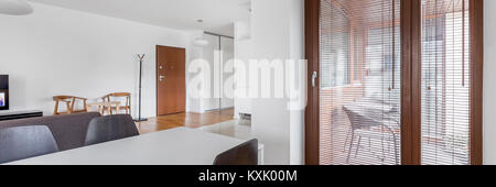 Appartement moderne avec table blanche et les portes de balcon avec stores en bois, panorama Banque D'Images