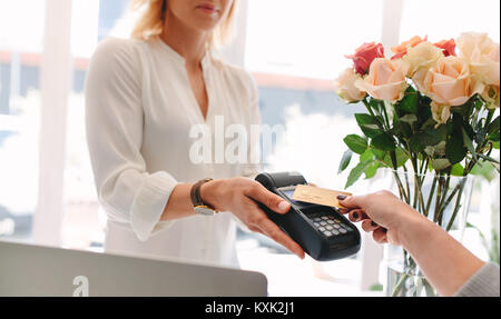 Client déposant le paiement sans contact avec la technologie NFC carte de crédit au magasin de fleur. Cropped shot en mettant l'accent sur le paiement sans contact des mains. Banque D'Images