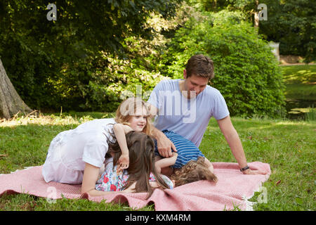 Young parents avec deux filles avant de flexion on picnic blanket in park Banque D'Images