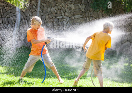 Les garçons en pulvérisation jardin les uns les autres avec de l'eau d'arrosage Banque D'Images