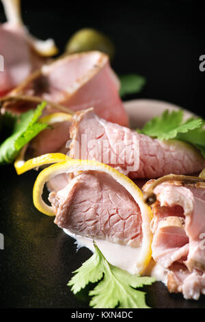 Vitello tonnato plat italien. Fines tranches de veau avec sauce au thon, les câpres et la coriandre servi sur la plaque noire. Close up Banque D'Images