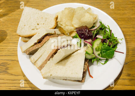 Collation au déjeuner rôti de bœuf maigre froid et oignons rouges chutney dans le pain blanc avec des chips de pommes de terre et salade de roquette Banque D'Images