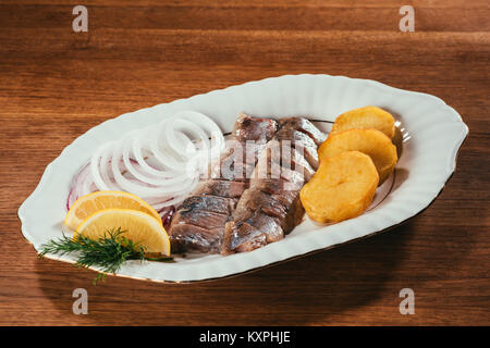 Tranches de poisson hareng portant sur la plaque avec l'oignon et les tranches d'orange sur la table en bois Banque D'Images