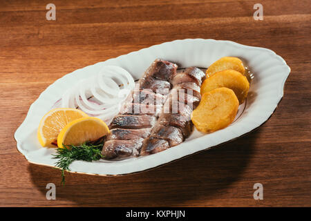 Tranches de poisson hareng portant sur la plaque avec l'oignon et les tranches d'orange sur la table en bois Banque D'Images