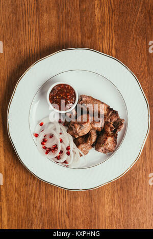 Vue de dessus de la viande grillée, sauce aux oignons et graines de grenade sur plaque blanche sur table en bois Banque D'Images