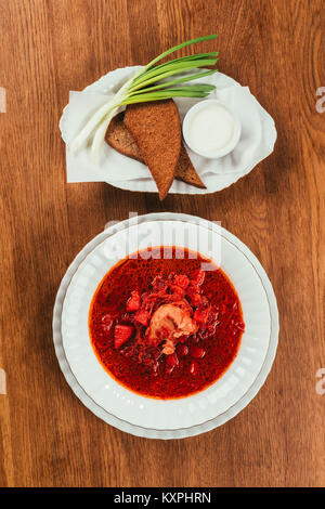 Vue de dessus de borscht lave en plaque blanche servi avec pain de seigle sur table en bois Banque D'Images