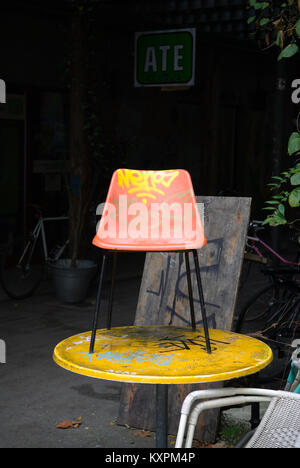 Une chaise en plastique moulé orange couverts de graffitis est situé au sommet d'un jaune graffitied table ronde. Dans l'arrière-plan on voit le mot "DATE" sur un panneau Banque D'Images