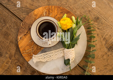 Une tasse de café noir et blanc et de lisianthus bouquet avec ranunculus jaune sur un demi-ronde en et demi-plaque en bois. Vue d'en haut. Banque D'Images