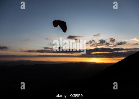 Beau coup d'une silhouette parapente voler au-dessus de Monte Cucco (Ombrie, Italie) avec le coucher du soleil sur l'arrière-plan, avec de belles couleurs et les tons sombres Banque D'Images