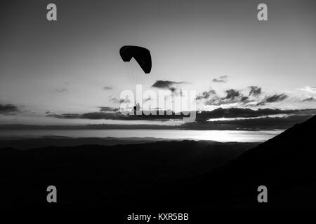 Beau coup d'une silhouette parapente voler au-dessus de Monte Cucco (Ombrie, Italie) avec le coucher du soleil sur l'arrière-plan Banque D'Images