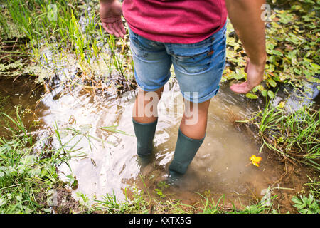 Teenage boy en bottes de caoutchouc dans le lac permanent. Banque D'Images