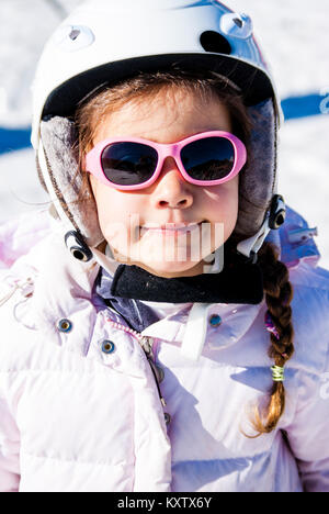 5 ans, fille habillée pour aller faire du ski avec casque et lunettes, habillé en blanc et rose a l'air à l'intérieur de l'appareil Banque D'Images