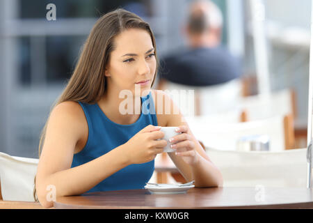 Femme sérieuse réflexion et tenant une tasse assis dans un bar terrasse Banque D'Images