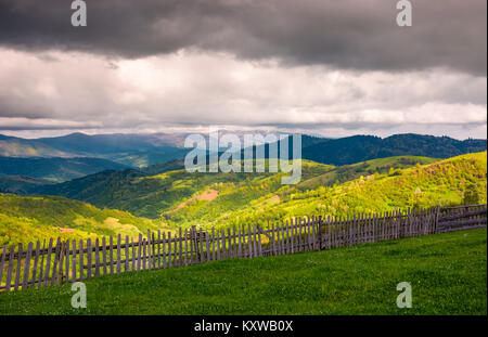 Clôture en bois le long de la colline herbeuse. beau printemps paysage de montagnes des Carpates un jour nuageux. Banque D'Images