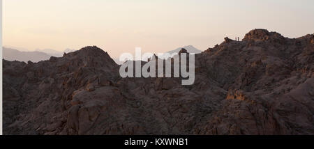 Deux personnes dans la distance debout au sommet d'une montagne dans la lumière du soir ayant une photo prise. Banque D'Images