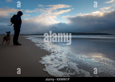 Man Walking dog sur Grand Strand Beach dans la belle lumière du soir en hiver, l'île d'Islay, Ecosse Banque D'Images