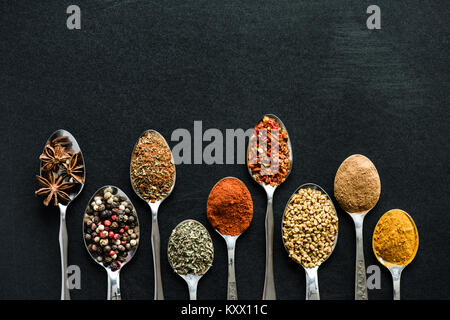 Vue de dessus de différentes épices et herbes dans les cuillères métalliques isolated on black Banque D'Images