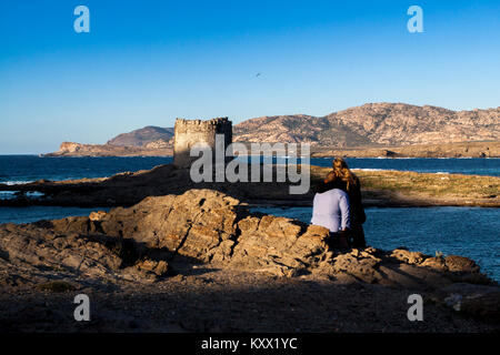 Vue arrière d'un couple sur les rochers à la recherche à travers la mer au phare abandonné au crépuscule. La Pelosa, Sardaigne. Italie Banque D'Images