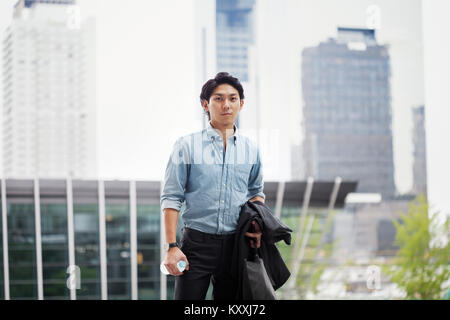 Businessman wearing blue shirt standing outdoors, holding jacket, serviette et bouteille d'eau. Banque D'Images