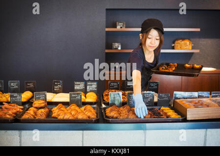 Femme travaillant dans une boulangerie, en plaçant des croissants frais et des gâteaux sur les grands plateaux sur un compteur. Banque D'Images