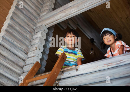 Low angle view of boy et de la jeune fille aux cheveux noirs à l'échelle de fenêtre, appuyé contre la paroi en bois. Banque D'Images